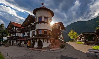 A picturesque building in Bavarian style with a round tower. The sun shines behind the clouds, illuminating the surroundings.