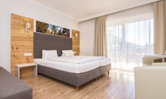 A modern bedroom with two single beds and a large window. The room is bright and stylishly furnished, featuring wooden paneling and a cozy seating area.