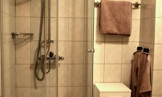A modern shower cabin with a glass door in a tiled bathroom. Next to the shower, there is a small cabinet, and towels are hanging on the wall.