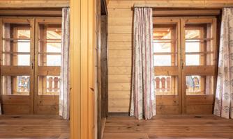 A cozy room with wooden walls and large windows. The windows are adorned with curtains and offer a lovely view outside.
