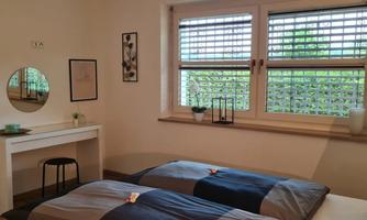 A cozy bedroom with two beds and a desk.  
Large windows provide plenty of daylight and a view of the greenery.