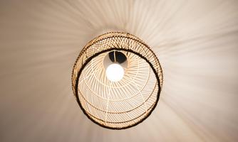 A stylish ceiling light made of rattan with a central bulb design. The light gently radiates and creates shadow patterns on the ceiling.