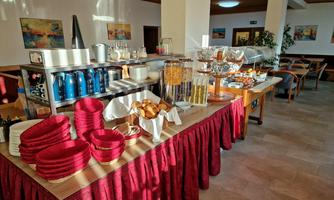 A buffet with various foods and drinks is ready. Red tablecloths and an inviting atmosphere characterize the room.