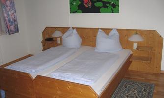 A cozy bedroom with a wooden double bed and two pillows. Pictures hang on the walls, and there are two nightstands with lamps.