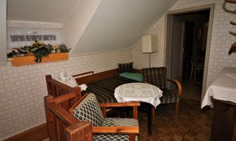 A cozy living space with a sofa, two chairs, and a table. The walls are light and decorated with a simple pattern.