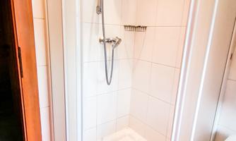 A modern shower cabin with glass walls and a hand shower. The walls are tiled and the floor tiles are in a warm color shade.