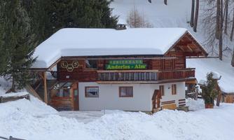 A cozy wooden house in the snow is situated in a winter landscape. Surrounded by trees, it offers an inviting atmosphere for visitors.