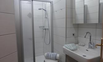 A modern bathroom with a shower cabin and a sink. The walls are tiled with light tiles, and a towel is ready.