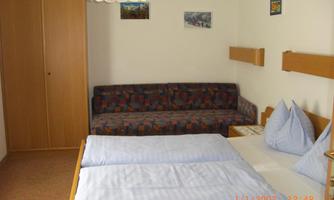 A simple room with a double bed and a sofa bed. Several pictures hang on the walls, and there is a large wardrobe.