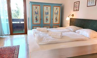 A cozy bedroom with a double bed and fresh towels. A blue wardrobe and a window with a balcony view create an inviting atmosphere.