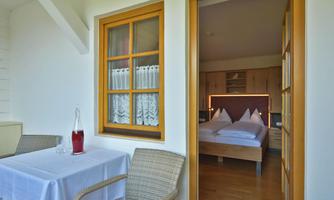 A cozy balcony with a table and chairs, overlooking a bright bedroom. The room is inviting and tastefully decorated.