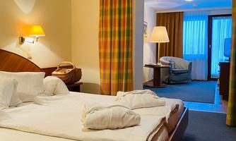 A comfortable hotel room with a double bed and cozy furnishings. The window offers a view of a bright living area.