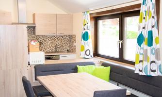 A modern kitchen with a dining area and large windows. The colors of the curtains are bright and vibrant, combined with neutral wood and gray tones.