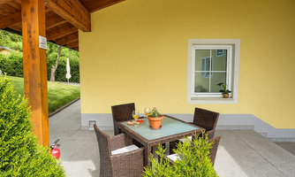 A cozy table with chairs is set on a terrace in front of a yellow wall. The table has drinks and a plant on it.