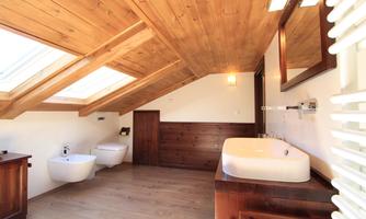 A modern bathroom with slanted wooden ceilings and large windows. It features an elegant washbasin and stylish wooden constructions.