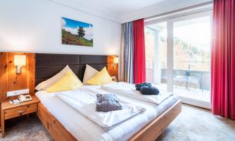 A cozy bedroom with a large bed and yellow cushions. Large windows let in plenty of light and provide access to a balcony.