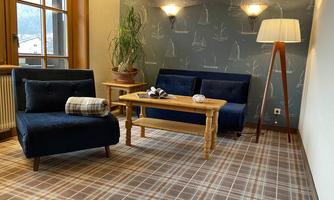 A cozy living area with two blue sofas and a wooden coffee table. The walls are decorated with maritime motifs, and a large plant pot as well as a floor lamp add warmth to the room.