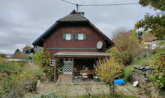 A traditional, red-painted house with a hipped roof. The garden is green and surrounded by trees and bushes.