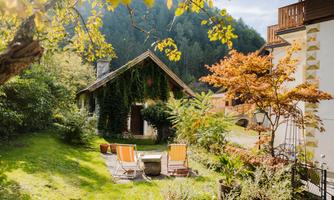 A picturesque garden with a wooden gazebo and two loungers. Surrounded by lush greenery and colorful plants, the scene radiates tranquility and coziness.
