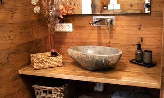 A modern bathroom with wooden paneling and an elegant stone sink. The decor is minimalist and inviting, with natural decorations and towels.
