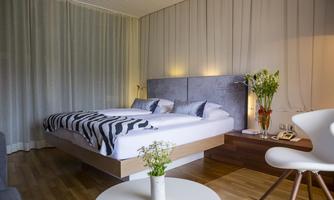 A cozy bedroom with a large double bed and modern design. The room is bright and friendly, with a small table and fresh flowers.