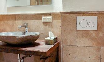 A modern bathroom with a stylish washbasin and a white toilet. The space is equipped with warm tones and bright lighting.