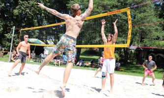 A group is playing volleyball. They are in athletic clothing and enjoying a sunny day outdoors.