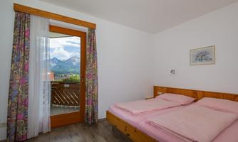 A cozy bedroom with two beds and a large window. The view shows a beautiful mountain landscape.
