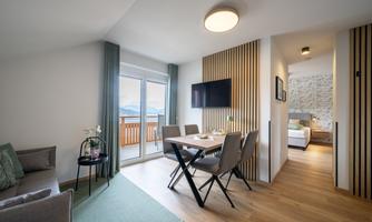 A modern kitchen with a dining area and a sofa. Large windows provide plenty of light and a beautiful view.