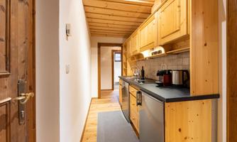 A modern kitchen with wooden cabinets and stainless steel appliances. The long hallway has a clean, inviting style.