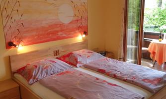 A cozy bedroom with two single beds and colorful bedcovers. In the background, a balcony with a table and chairs can be seen.