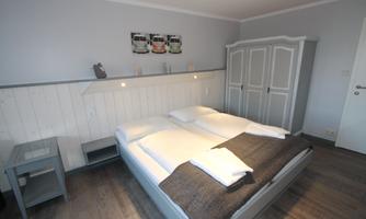 A bright bedroom with a double bed and two bedside tables. The walls are in soft shades of gray and a wardrobe is on the side.