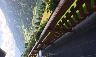 A beautiful balcony with a wooden fence and a view of a green mountain landscape. In the background, hills and a lake can be seen.
