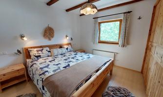 A cozy bedroom with a large wooden bed and animal-patterned duvet cover. Bright windows let in plenty of light, and the wooden details create a warm atmosphere.