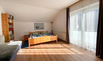 A bright bedroom with a wooden bed and a comfy couch. Large windows let in plenty of daylight.