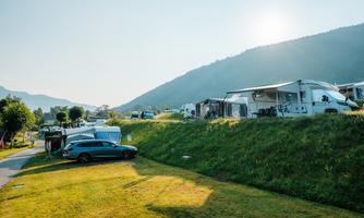 A sunny campsite with campervans and green grass. In the background, gentle mountains are visible.