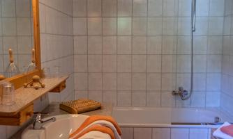 A bright bathroom with a bathtub and a shower. The room has wooden details and a pleasant atmosphere.