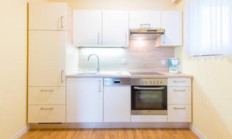 A modern kitchen with white cabinets and a wooden countertop. It features a stove, a dishwasher, and a sink.