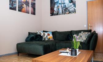 A cozy living room with a green couch and a wooden coffee table. Pictures of city views hang on the wall.