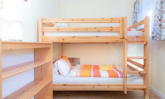 A cozy children's room with a bunk bed made of light wood. The walls are painted in a friendly manner, and a shelf is located next to the bed.