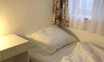 A simple bedroom with a bed and a bedside table. The walls are light, and a picture of snowy trees hangs on the wall.