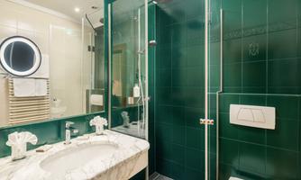 A modern bathroom with green tiles and an elegant marble sink. The shower is separated by a glass partition and a round mirror is mounted on the wall.