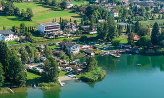 A picturesque landscape with a serene lake and green meadows. Small buildings and boats at the shore create an inviting atmosphere.