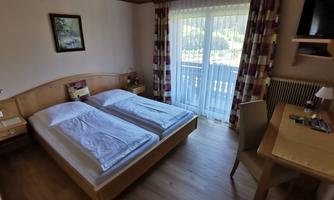 A cozy room with two single beds and a desk. Large windows let in plenty of daylight and provide access to a balcony.