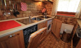 A cozy kitchen with wooden furniture and a sink. In the foreground, a dishwasher and a washing machine are visible.