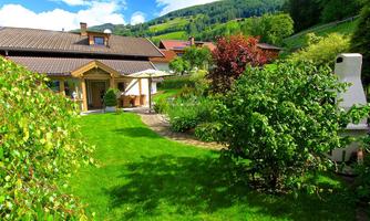 A cozy house with a beautiful garden. The garden is green, with various plants and an idyllic landscape in the background.