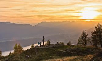 A breathtaking sunset over the mountains with a group of people in front of a wooden cross. The landscape is peaceful and full of natural beauty.