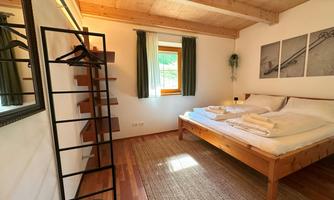 A cozy bedroom with a large bed and wooden details. The windows let in a lot of light and offer a view outside.