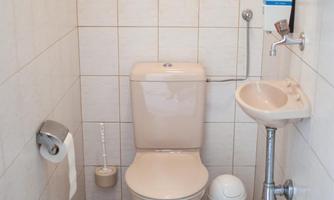 A small bathroom with a toilet and a sink. The walls are tiled and the floor has a carpet.