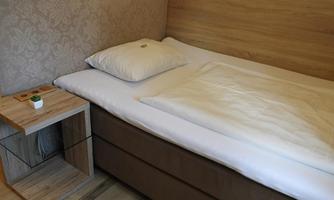 A simple bedroom with a single bed and a wooden bedside table. The walls are painted in a warm color tone.